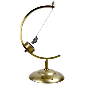 May include: A gold-colored metal stand with a curved arm and a small, dark gray object hanging from it. The stand has a round base with a small plaque that reads "The Moon, 1969".