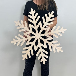 May include: A large, wooden snowflake cutout. The snowflake is a simple design with six points and is made of light-colored wood.