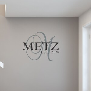 May include: A gray wall with a black and gray vinyl decal that says "METZ EST. 1994". The decal features a stylized letter "M" with a decorative flourish.