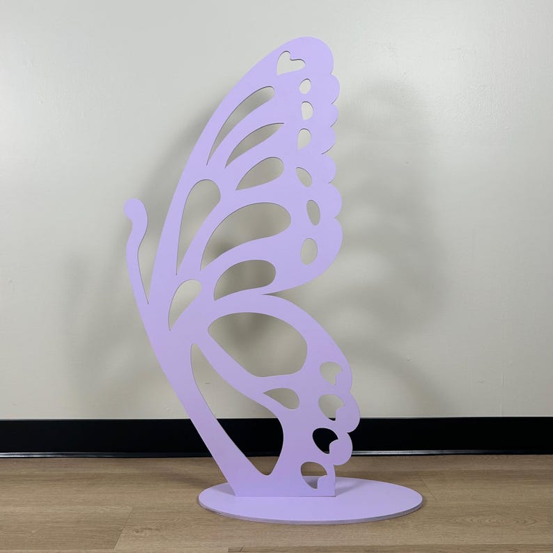 May include: A large, lavender-colored butterfly cutout, standing on a round base. The butterfly has intricate details and a delicate design.