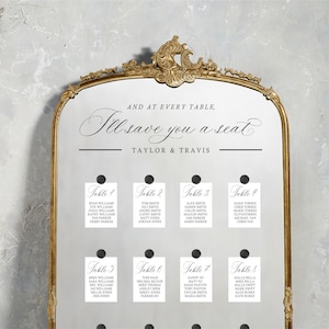 May include: A white wedding seating chart with black text. The chart is titled "And at every table, I'll save you a seat" with the names "Taylor & Travis" below. The chart is divided into eight tables with a list of names for each table.