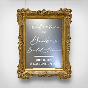 May include: A gold-framed mirror with a white inscription that reads "Welcome to Brilee's Bridal Shower July 16, 2022 55 Days Until "I Do""