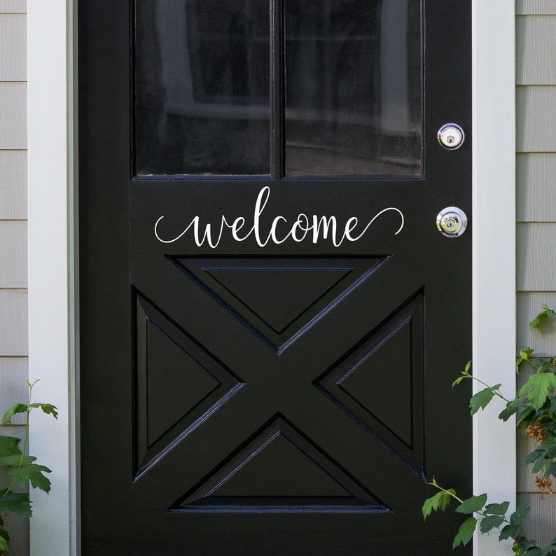 Puede incluir: Una puerta delantera negra con un letrero blanco de "bienvenida" y un dise&ntilde;o decorativo en forma de X. La puerta tiene dos pomos de puerta plateados.