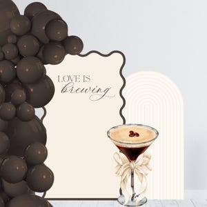 May include: A brown and beige printable backdrop with the text "Love is brewing" and a coffee cocktail illustration. The backdrop is decorated with a brown balloon garland.