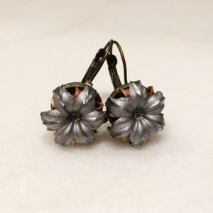 May include: A pair of silver bullet earrings with a flower design. The earrings are made from real bullet casings and have a bronze-colored hook.