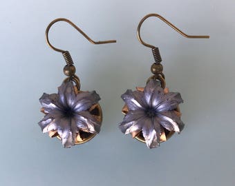 May include: A pair of handmade earrings featuring a unique floral design. Each earring showcases a silver-colored, flower-shaped element with a brass-colored base, suspended from a brass-toned hook.