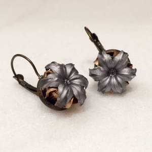 May include: A pair of silver and gold earrings featuring a flower design made from spent bullet casings.