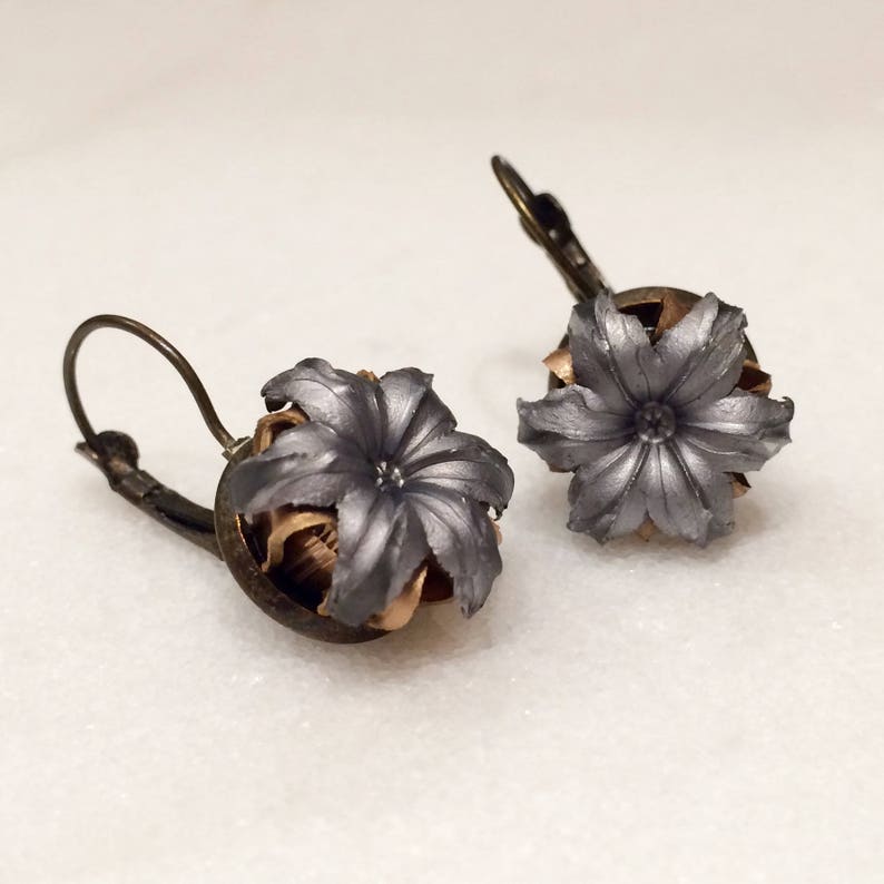 May include: A pair of silver and gold earrings featuring a flower design made from spent bullet casings.