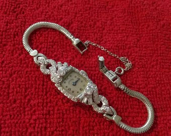 Könnte beinhalten: Eine silberne Armbanduhr mit weißem Zifferblatt und Diamantbesatz. Die Uhr hat ein silbernes Armband mit einem Kettenverschluss.
