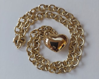 May include: A gold chain necklace with a heart-shaped pendant. The chain is a classic link style and the pendant is smooth and shiny.