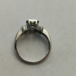 May include: A silver ring with a large, faceted, multi-colored gemstone in the center. The ring has a simple band.
