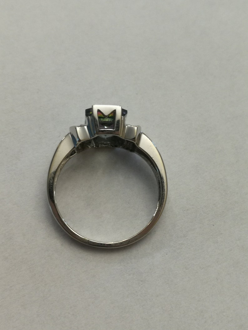May include: A silver ring with a large, faceted, multi-colored gemstone in the center. The ring has a simple band.