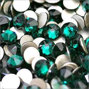 Puede incluir: Primer plano de una gran cantidad de piedras de imitación de color verde esmeralda con respaldo plateado. Las piedras de imitación están dispuestas en un patrón aleatorio.