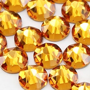 Puede incluir: Primer plano de un grupo de pequeños diamantes de imitación redondos de color ámbar. Los diamantes de imitación tienen un diseño facetado y están dispuestos en un patrón aleatorio.