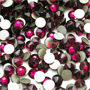 Op de afbeelding: Een close-up van een stapel kleine, ronde, fuchsia-kleurige strasssteentjes met zilveren zelfklevende achterkanten.