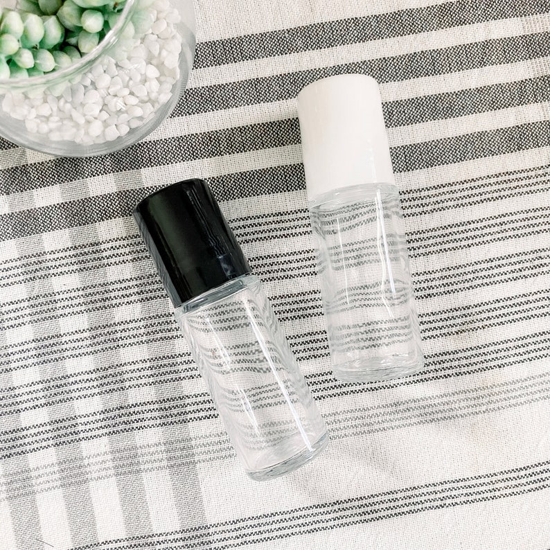 May include: Two clear glass roller bottles with black and white caps. The bottles are on a white and gray striped fabric.
