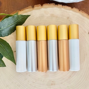 Könnte beinhalten: Sechs goldfarbene Roll-on-Flaschen mit verschiedenen Flüssigkeiten im Inneren. Die Flaschen sind auf einer Holzoberfläche aufgereiht.