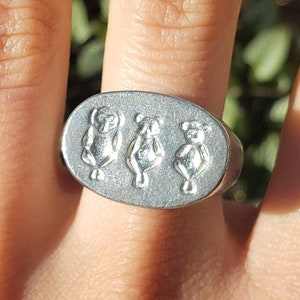 Peut inclure: Une bague en argent avec trois ours en rangée sur le dessus. Les ours sont tournés vers l'avant et ont les bras levés.