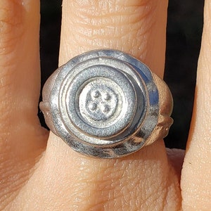 May include: A silver ring with a circular design featuring a raised, four-leaf clover motif.