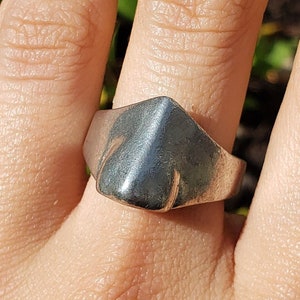 May include: A silver ring with a triangular shaped top. The ring is worn on a person's finger.