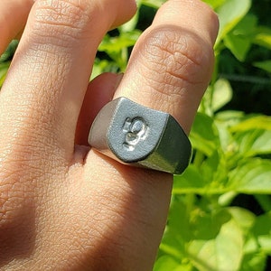 May include: A silver signet ring with a raised design on the top. The ring is worn on a person's finger.