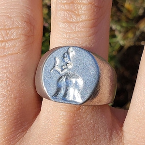 May include: A silver ring with a raised design of a woman holding a flower.