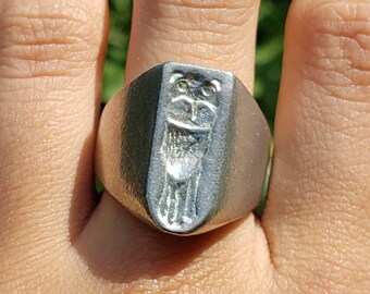 May include: A silver ring with a raised design of a stylised owl on the face of the ring.