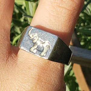 May include: A silver ring with a raised design of an elephant on the top. The ring is worn on a person's finger.