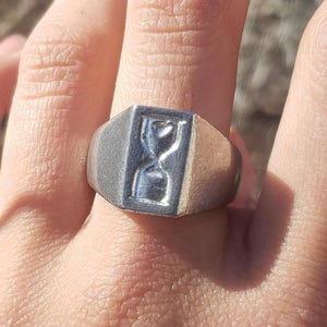 May include: A silver signet ring with an hourglass design.
