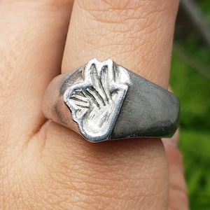 Peut inclure: Une bague en argent avec un motif en relief d'une main faisant le signe 'ok'.