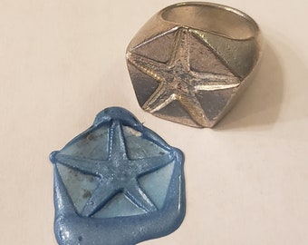 May include: A silver ring with a five-pointed star design. The ring is used to create a wax seal with a blue impression of the star.