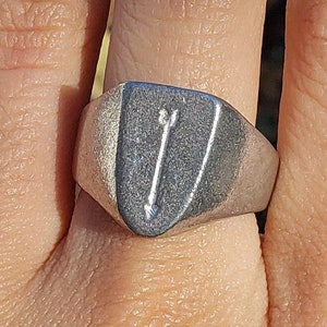 Op de afbeelding: Een zilveren ring met een schildvormig ontwerp met twee pijlen die naar boven wijzen.