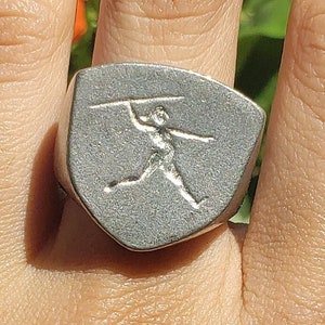 May include: A silver ring with a shield-shaped design featuring a figure throwing a javelin.