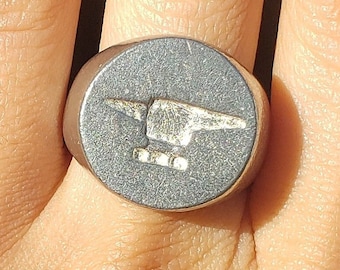 May include: A silver ring with a black oval-shaped stone featuring a raised image of an anvil.
