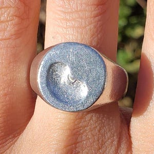 Puede incluir: Un anillo de sello de plata con una parte superior lisa y redondeada y un diseño en forma de corazón ligeramente elevado.