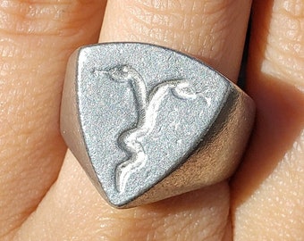 May include: A silver ring with a triangular face featuring a raised design of two snakes intertwined.