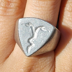 May include: A silver ring with a triangular face featuring a raised design of two snakes intertwined.