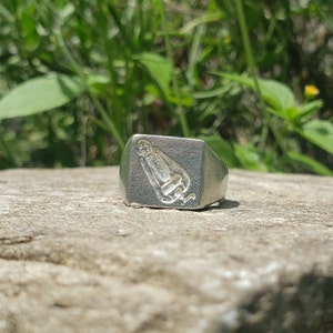 May include: A silver signet ring with a detailed image of a monkey sitting down.