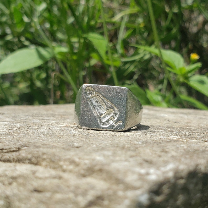 May include: A silver signet ring with a detailed image of a monkey sitting down.