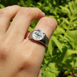 Peut inclure: Une bague en argent avec un motif détaillé sur le dessus. La bague est portée au doigt.