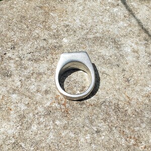 May include: A silver ring with a flat, wide band.