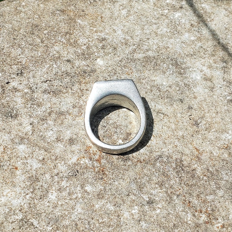 May include: A silver ring with a flat, wide band.
