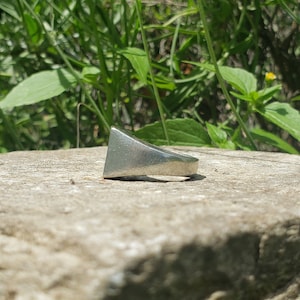 May include: A silver ring with a triangular shaped band.