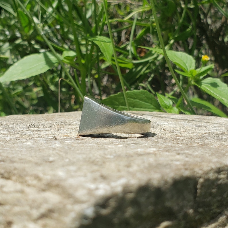 May include: A silver ring with a triangular shaped band.
