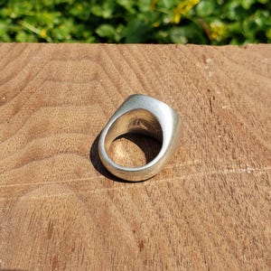 May include: A silver ring with a smooth, rounded top. The ring is sitting on a wooden surface.
