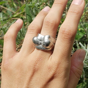 May include: A silver ring with a bow-shaped design. The ring is worn on a person's finger.
