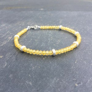 Könnte beinhalten: Ein zartes gelbes Perlenarmband mit silbernen Akzenten. Das Armband besteht aus kleinen, runden Perlen und hat ein schlichtes, elegantes Design.