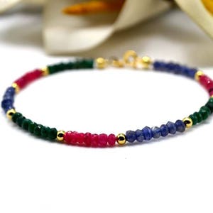 Pode incluir: Um bracelete delicado com contas de pedras preciosas verdes, rosa e azuis separadas por contas douradas. O bracelete tem um fecho dourado.