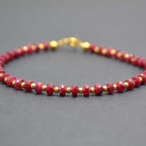Peut inclure: Un bracelet en pierres précieuses rouges avec des perles dorées. Le bracelet est composé de petites pierres précieuses rouges facettées et de perles dorées.