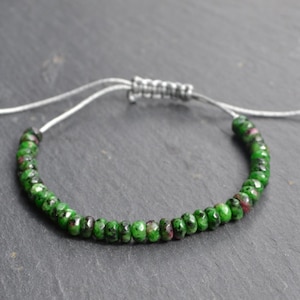 以下が含まれることがあります： 緑と赤の宝石のブレスレットで、銀色の調節可能なコードが付いています。